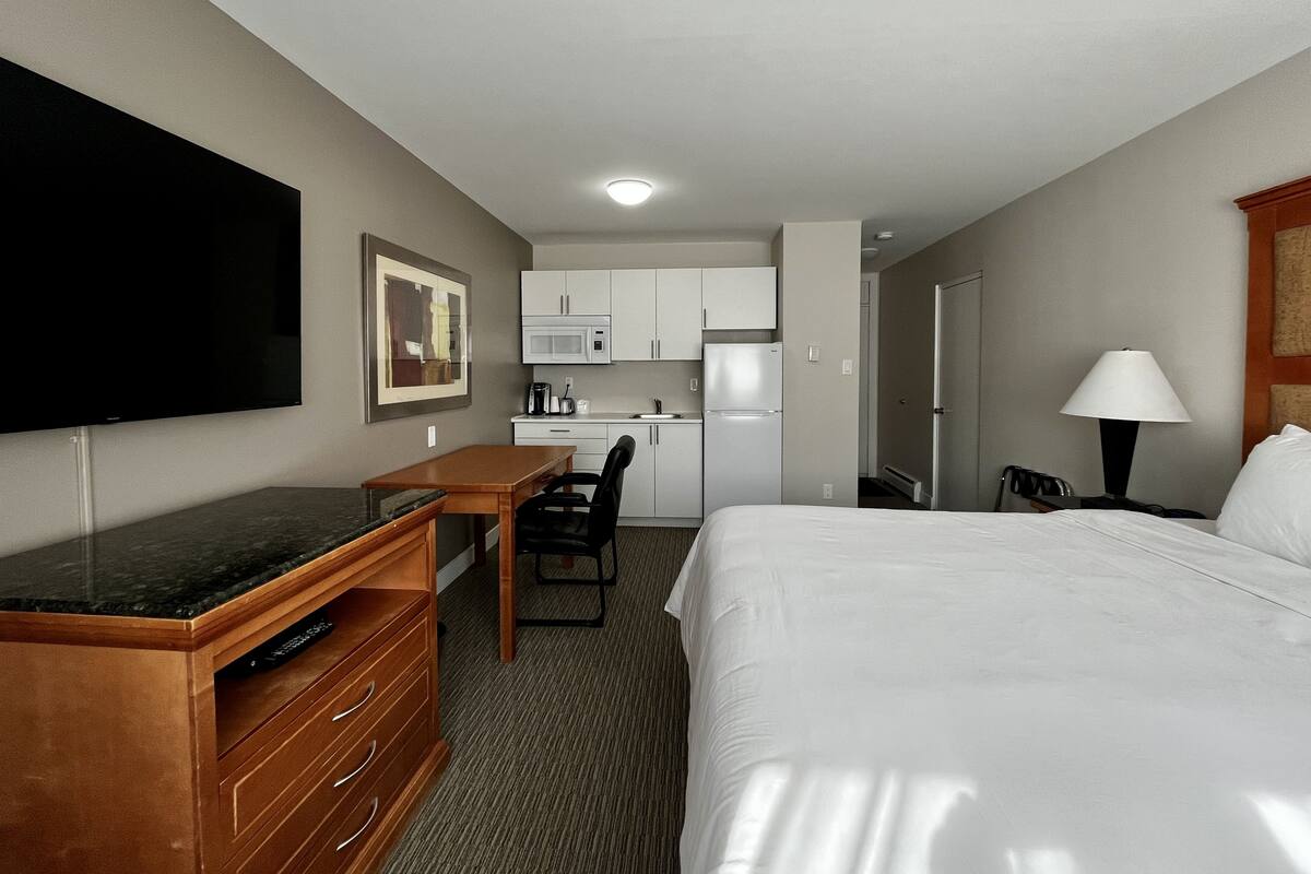 A hotel room with a bed, a desk with a flat-screen TV, a microwave, a refrigerator, and a lamp.