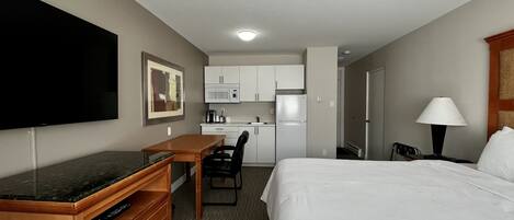 Una habitación de hotel con una cama, un escritorio con televisión de pantalla plana, un microondas, un refrigerador y una lámpara.