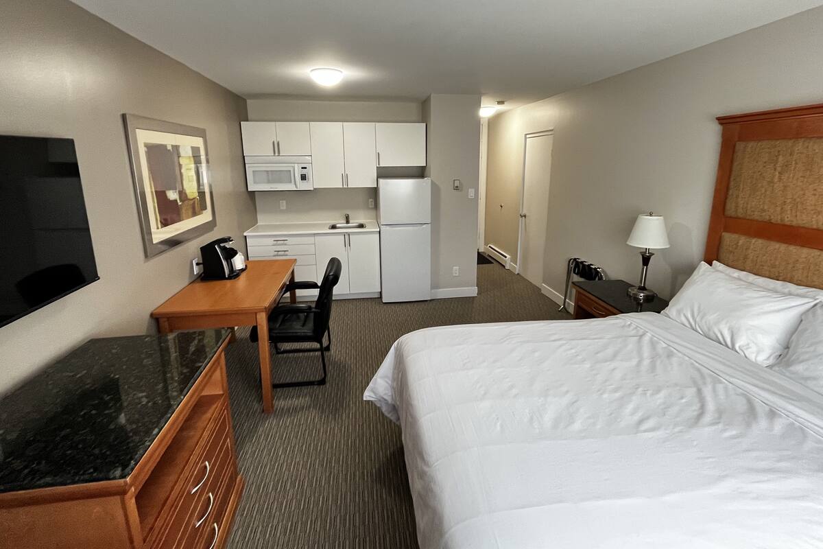 A hotel room with a bed, a desk, a chair, a microwave, a refrigerator, and a television.