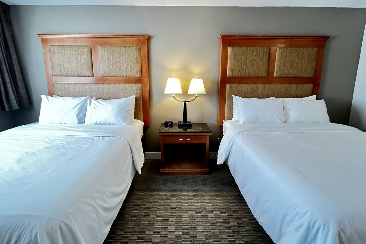 A hotel room with two beds, a nightstand with a lamp, and a carpeted floor.