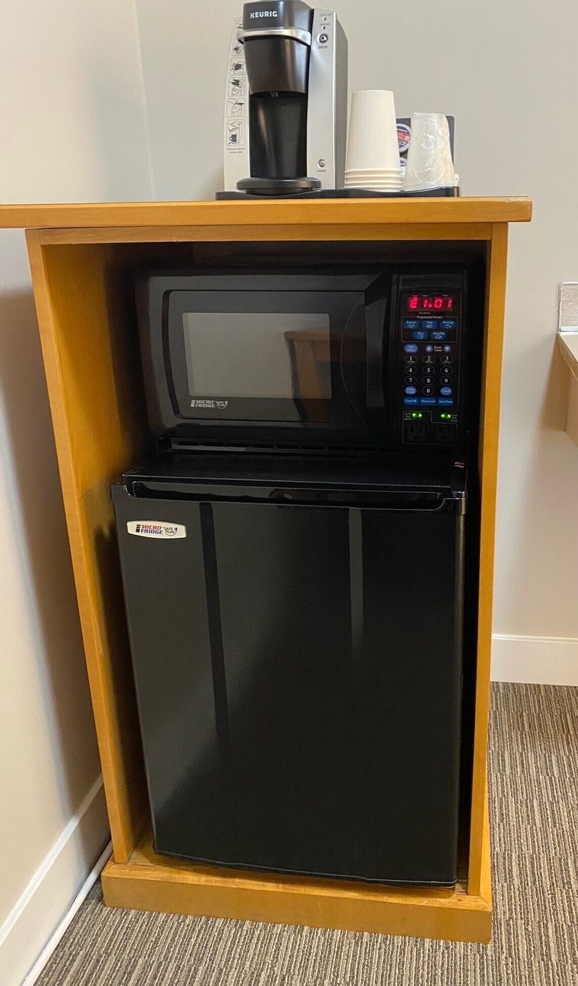 A compact kitchenette with a black refrigerator, a microwave, and a Keurig coffee maker.