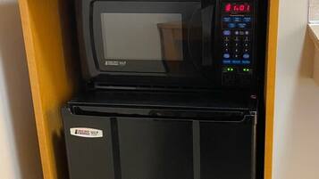 A compact kitchenette with a black refrigerator, a microwave, and a Keurig coffee maker.