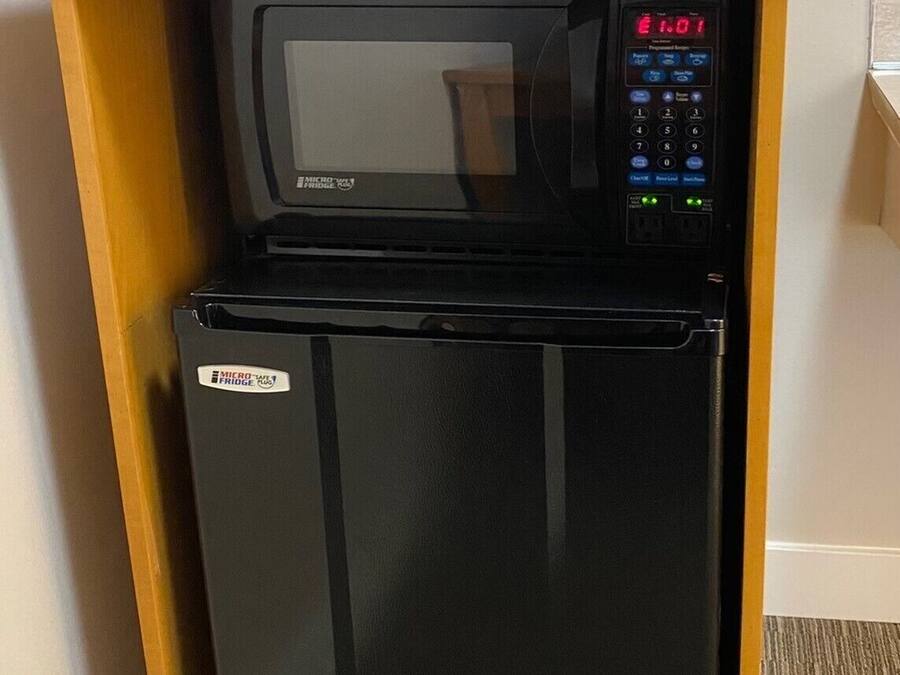 A compact kitchenette with a black refrigerator, a microwave, and a Keurig coffee maker.