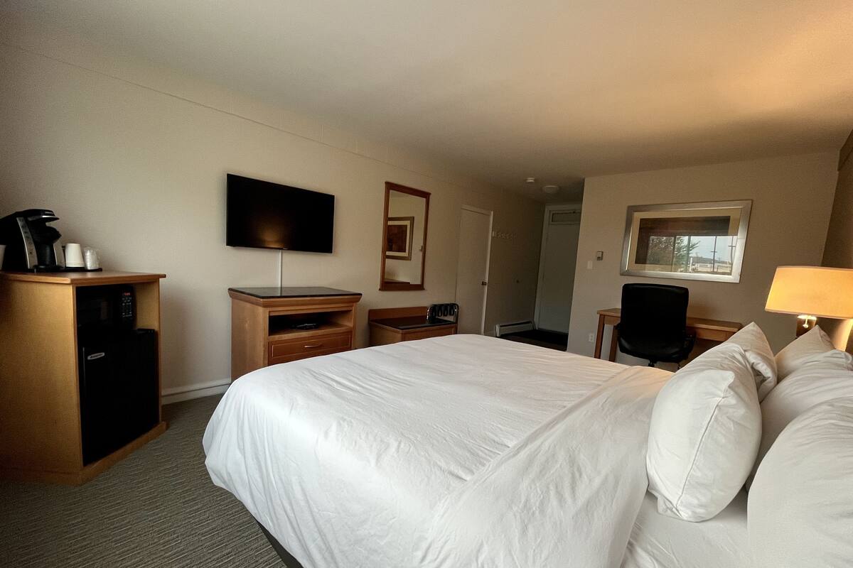 A hotel room with a large bed, a desk with a computer, a television, and a coffee machine.