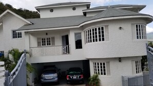 Een tweelaags huis met een garage, twee auto's binnen en een hekwerk ervoor.