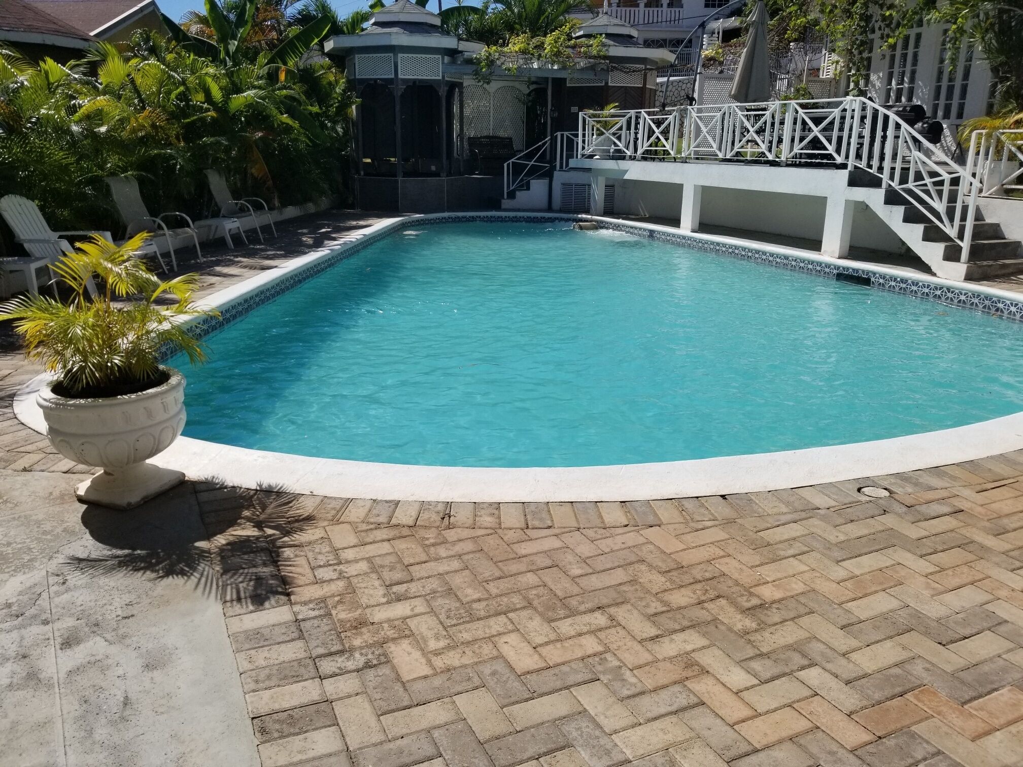 A rectangular swimming pool with a white edge, surrounded by a brick patio.