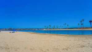 Una playa con agua cristalina azul, palmeras y una vista distante de edificios.