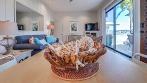 Una sala de estar moderna con una mesa de comedor de madera, un ventilador de techo, un televisor y un amplio ventanal con vistas al exterior.
