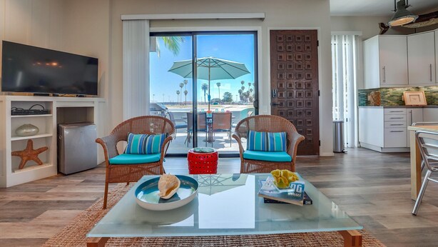 Una sala de estar con televisor, sillas de mimbre, una mesa de centro de vidrio y vistas al exterior.