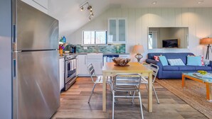 Una cocina moderna con refrigerador de acero inoxidable, gabinetes blancos y un comedor con mesa de madera y sillas de metal.