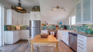 Una cocina moderna con armarios blancos, un refrigerador de acero inoxidable, una mesa de comedor de madera con sillas y una lámpara de techo original.