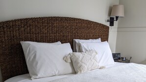 A neatly made bed with a textured white duvet and pillows, a woven headboard, and a bedside table with a lamp. - Luckystone Inn (Saugatuck)