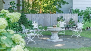 A patio with a stone table and four white metal chairs, surrounded by a wooden fence and greenery. - Luckystone Inn (Saugatuck)