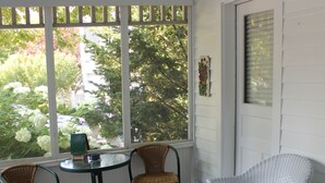 A room with a glass table, two wicker chairs, and a large window with a view of trees and a parked car. - Luckystone Inn (Saugatuck)