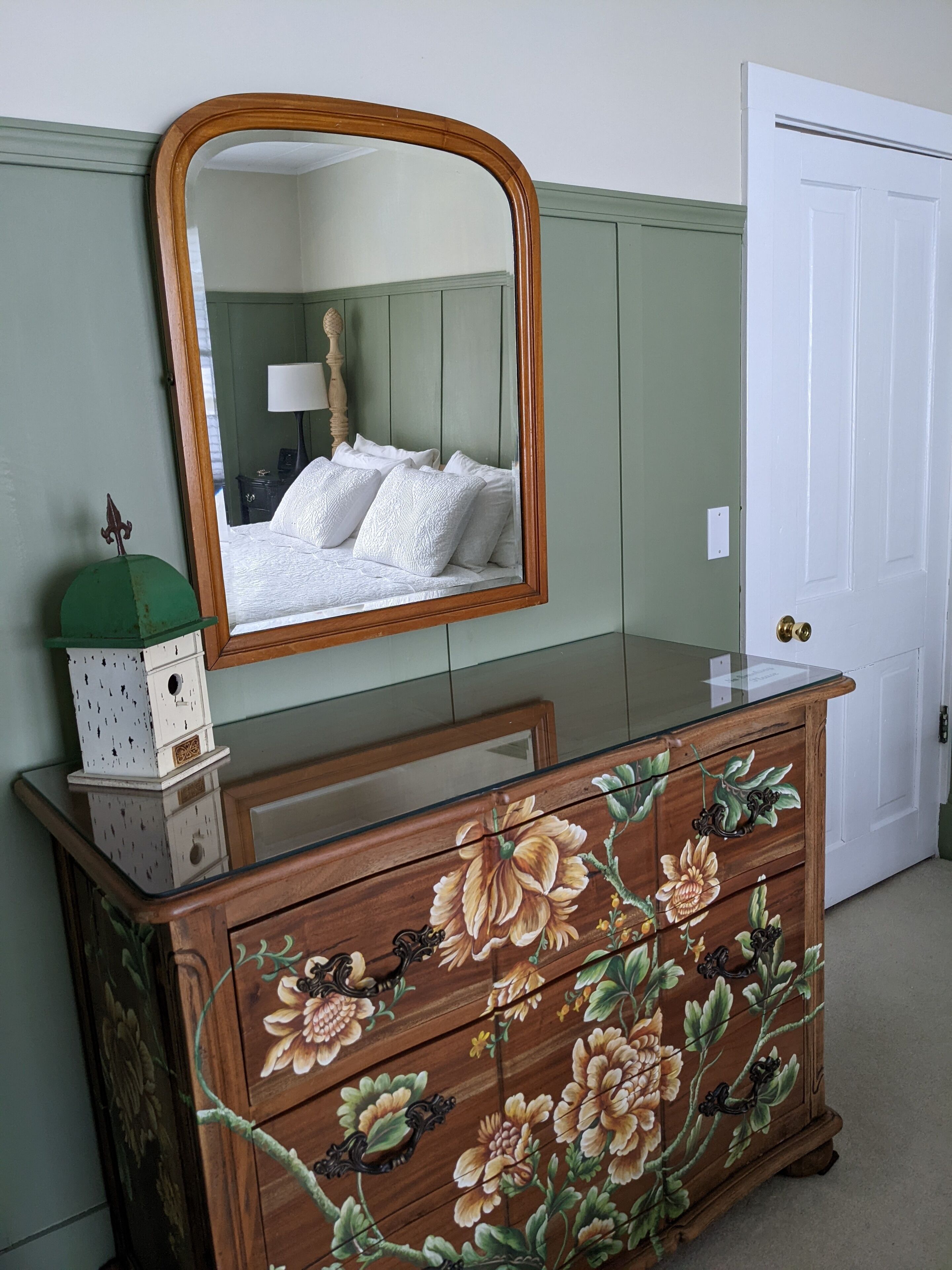 A wooden dresser with floral patterns, a mirror above it, and a white door in the background.