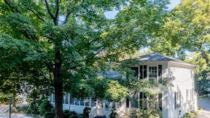 A white two-story house with a porch and a large tree in front. - Luckystone Inn (Saugatuck)