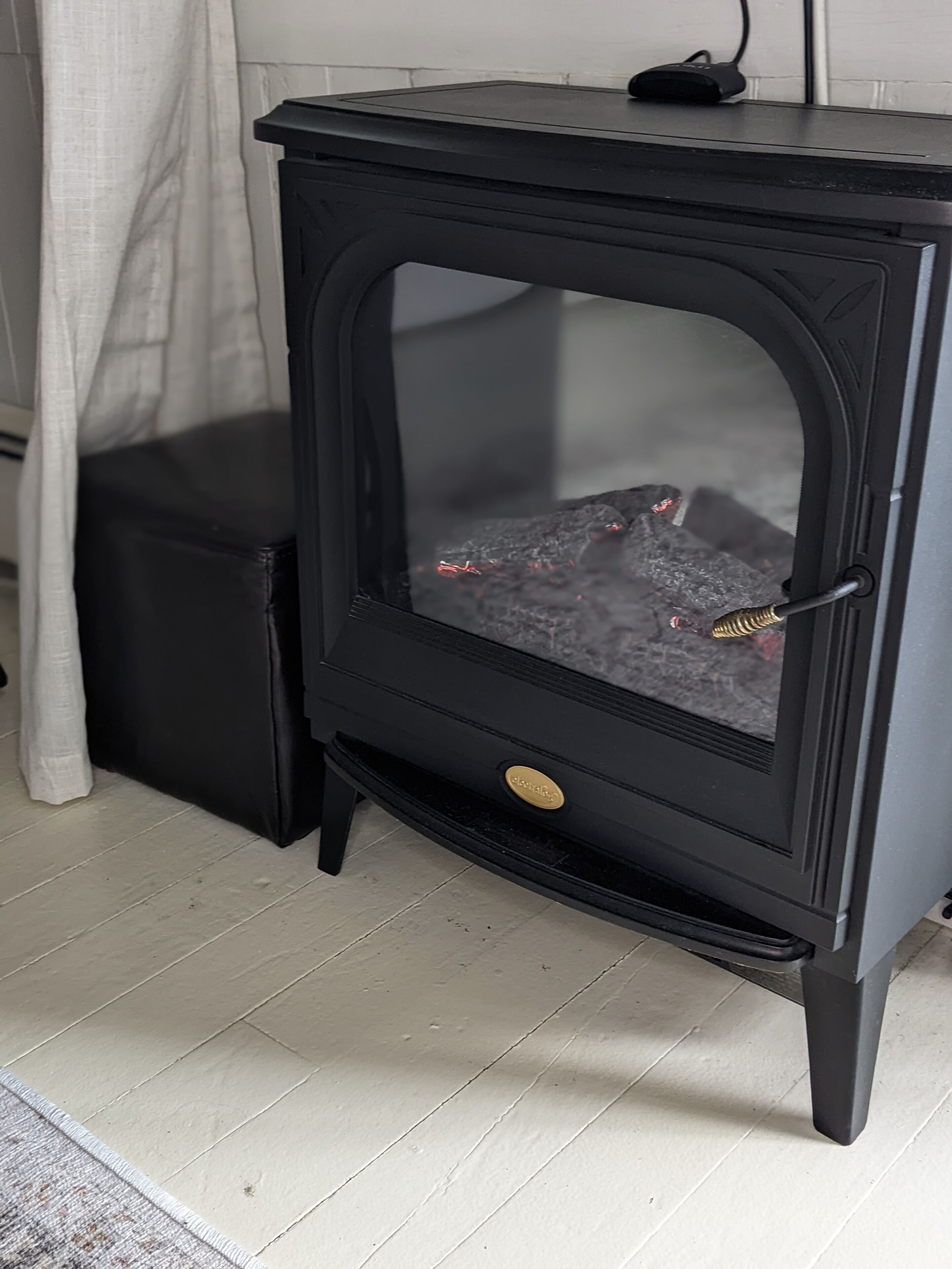 A black wood-burning stove with a glass door, a gold knob, and a black cord plugged in.