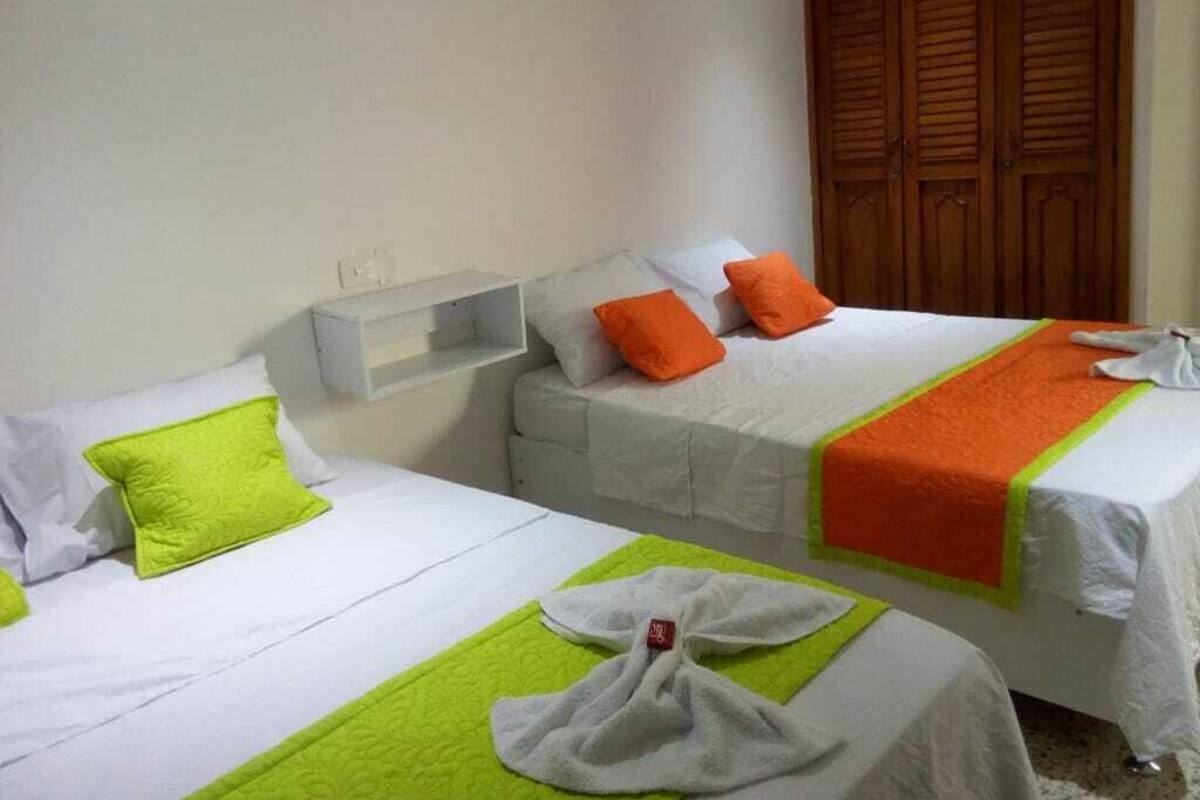 Deux lits simples avec du linge de lit blanc et des oreillers orange, une armoire en bois et une étagère blanche.