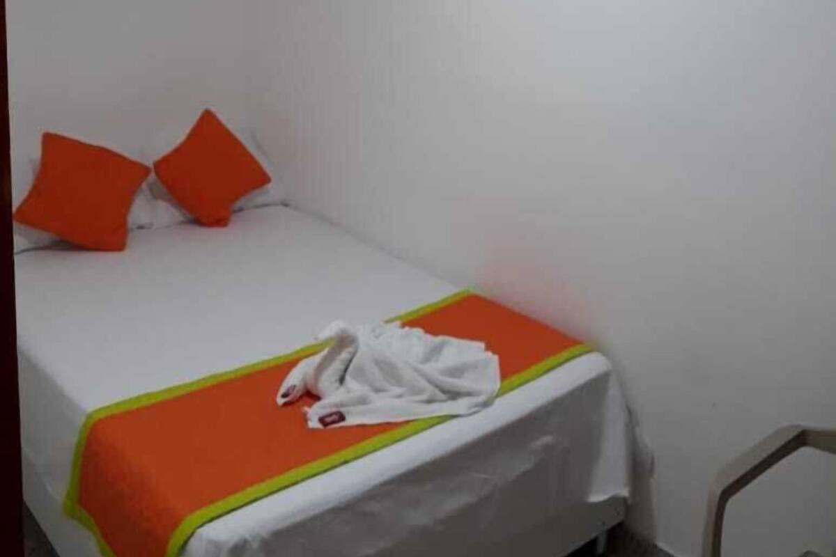 Un lit simple avec une couvre-lit et des oreillers orange, une couverture blanche et une serviette blanche sur le lit.