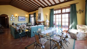 A dining area with a glass table, chairs, and a sofa. There are framed pictures on the walls and a lamp on the table. - Villa Altos de Santiago (Alajeró)