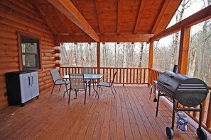 Une terrasse en bois avec une table et des chaises, un barbecue et un réfrigérateur.
