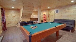 A wooden interior with a pool table, a sofa, and a bunk bed.