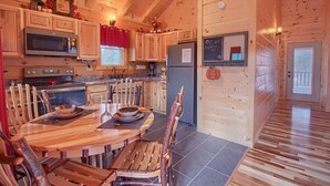 A wooden cabin interior with a dining area, kitchen, and a door with a chalkboard.
