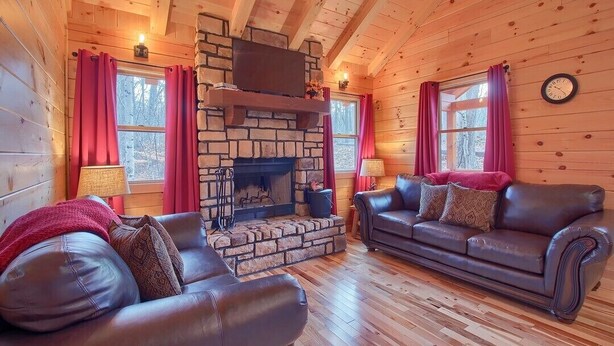 A cozy cabin interior with a stone fireplace, leather sofas, and wooden walls.