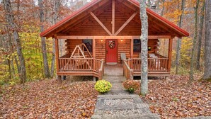 A log cabin with a red roof, wooden porch, and a front door.