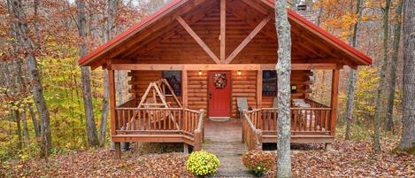 A log cabin with a red roof, wooden porch, and a front door.