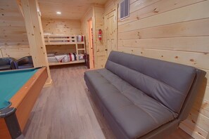 L’intérieur d’un chalet en bois comprend une table de billard, un canapé gris, des lits superposés et un extincteur.