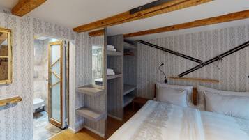Un dormitorio con cama, vigas de madera, armario y baño con inodoro y ducha.