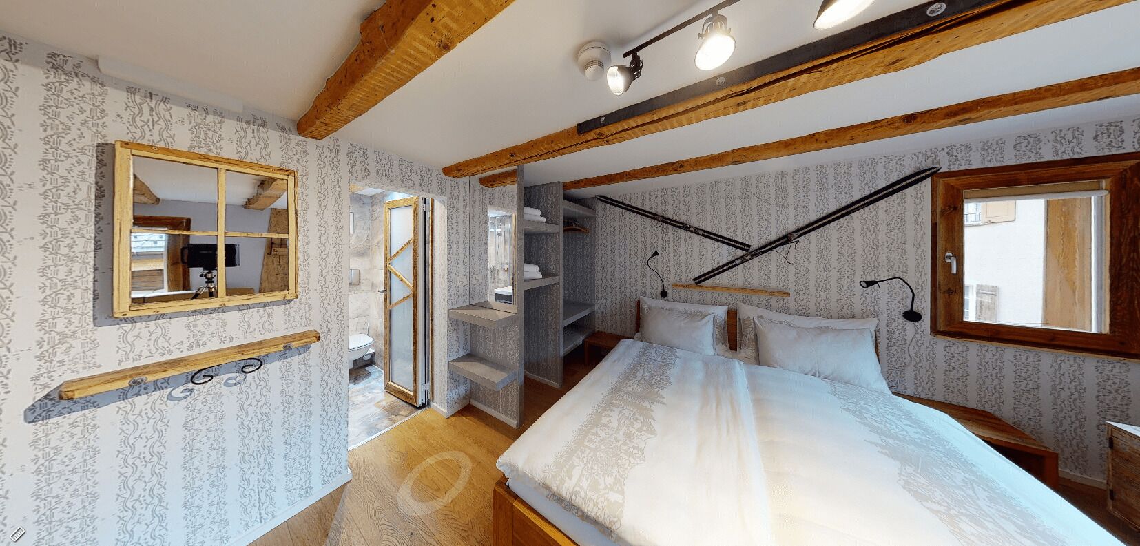 Ein Schlafzimmer mit einem großen Bett, Holzbalken, einem Spiegel und einem Fenster.