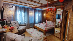 Ett mysigt rum med en säng, en soffa, ett matbord med en vas med blommor och ett träpanelat tak.