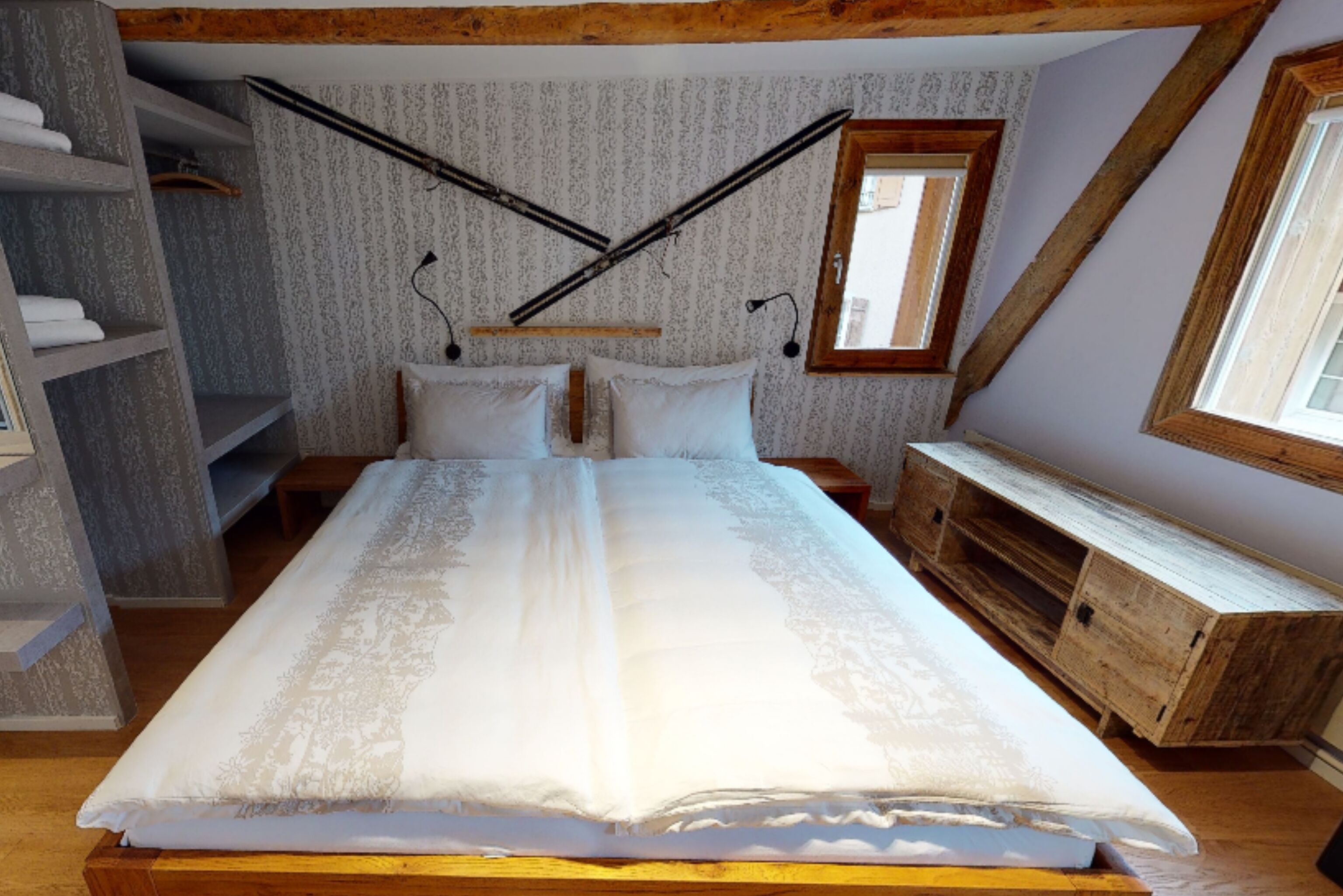 A bedroom with a large bed, wooden headboard, a wooden dresser, a wardrobe, and a window with a view.