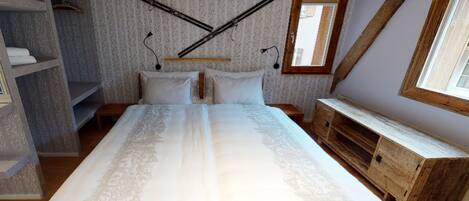 A bedroom with a large bed, wooden headboard, a wooden dresser, a wardrobe, and a window with a view.