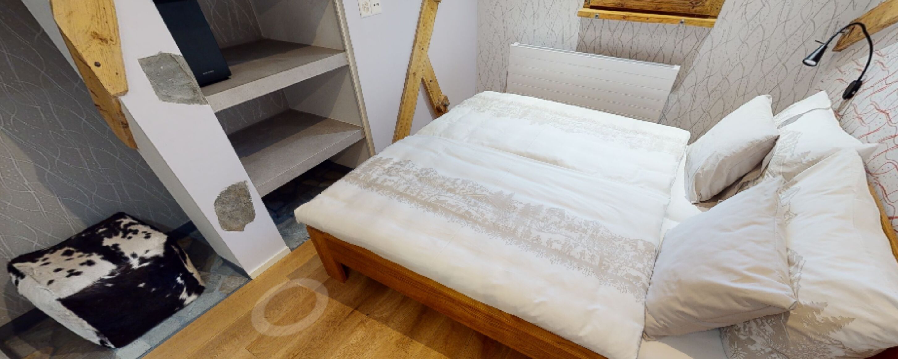 A bedroom with a wooden bed, white bedding, a small rug, and a patterned wall.