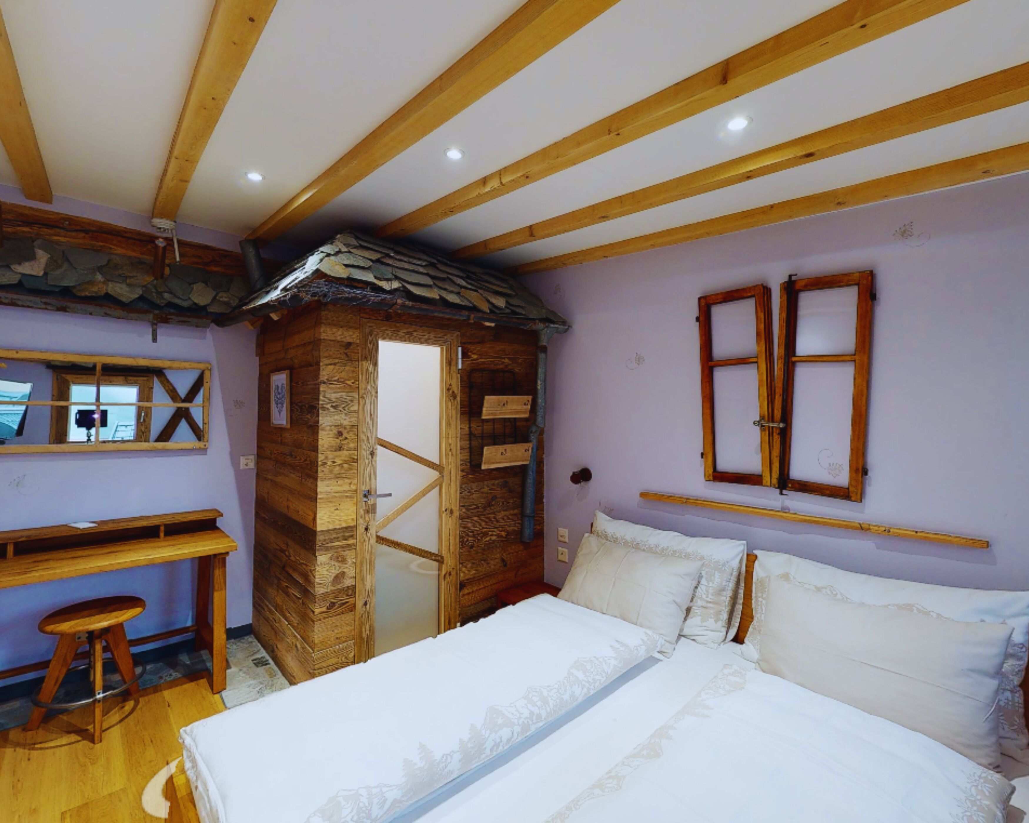 A rustic wooden cabin-style room with a bed, a small desk, and a stone wall.