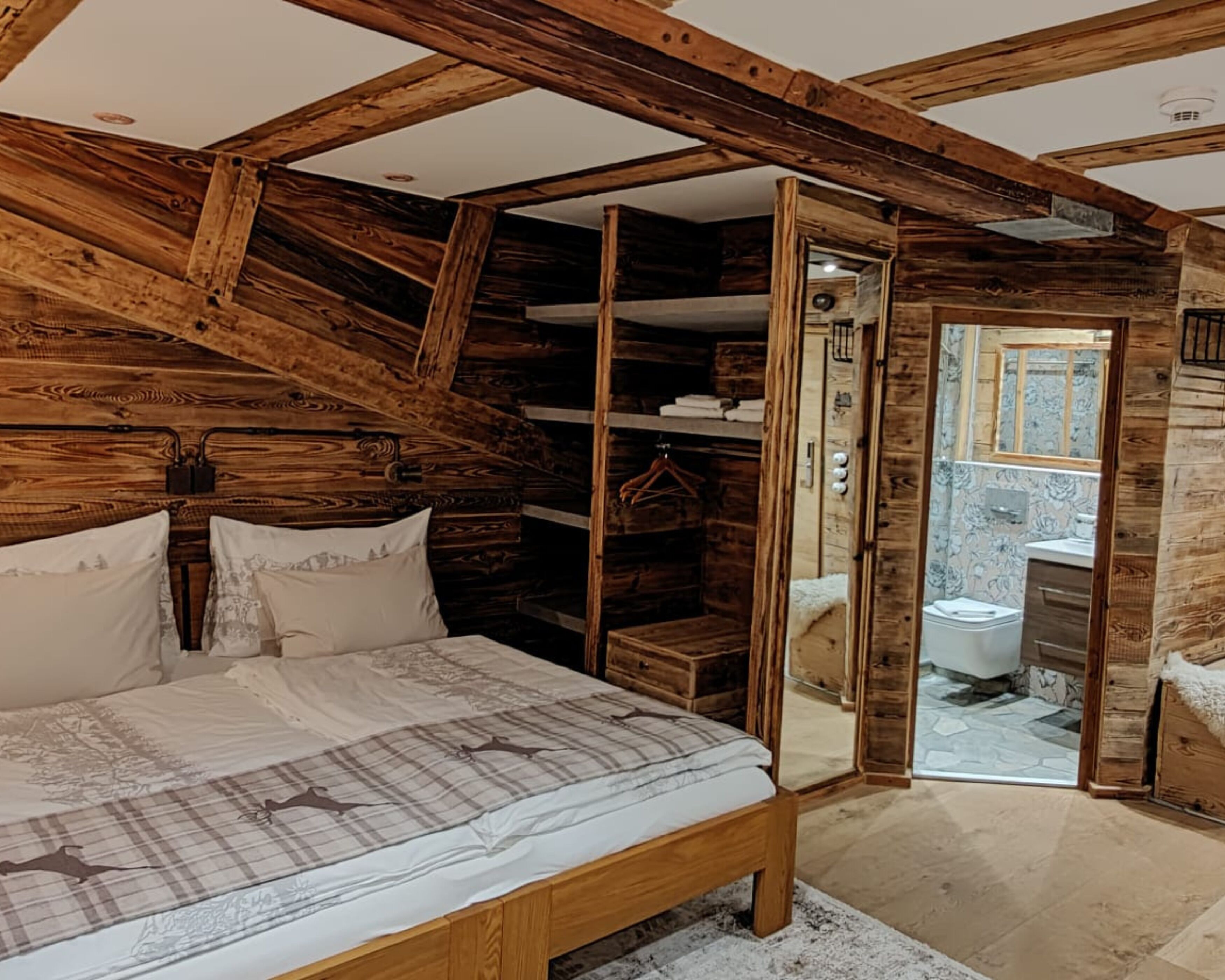 Un dormitorio rústico de madera con una cama grande, un vestidor y un baño visible a través de una puerta abierta.