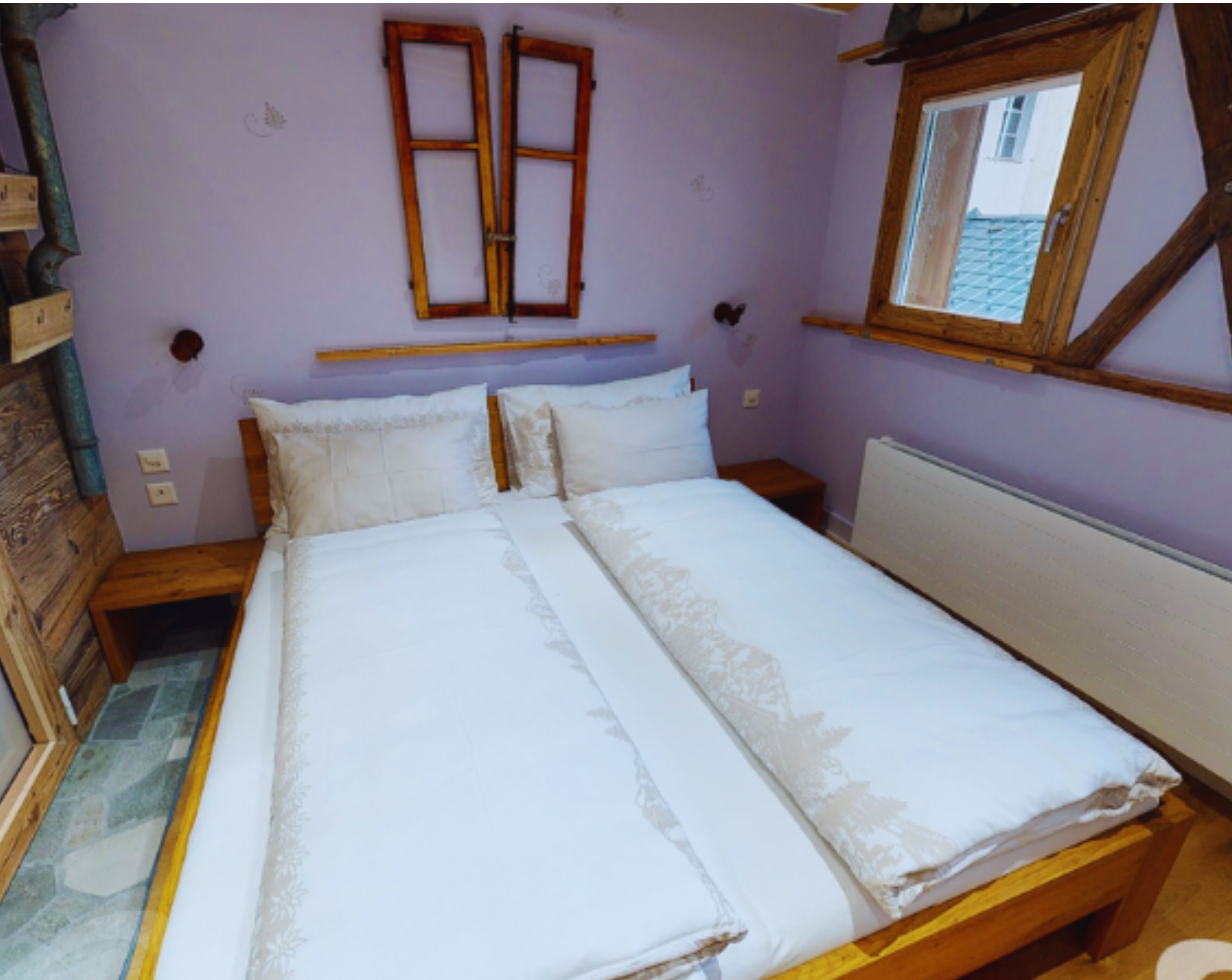 Une chambre à coucher avec un lit en bois, deux tables de chevet, une fenêtre avec un cadre en bois et un radiateur.