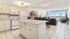Una cocina compacta con electrodomésticos blancos, una isla central y un comedor con vistas.