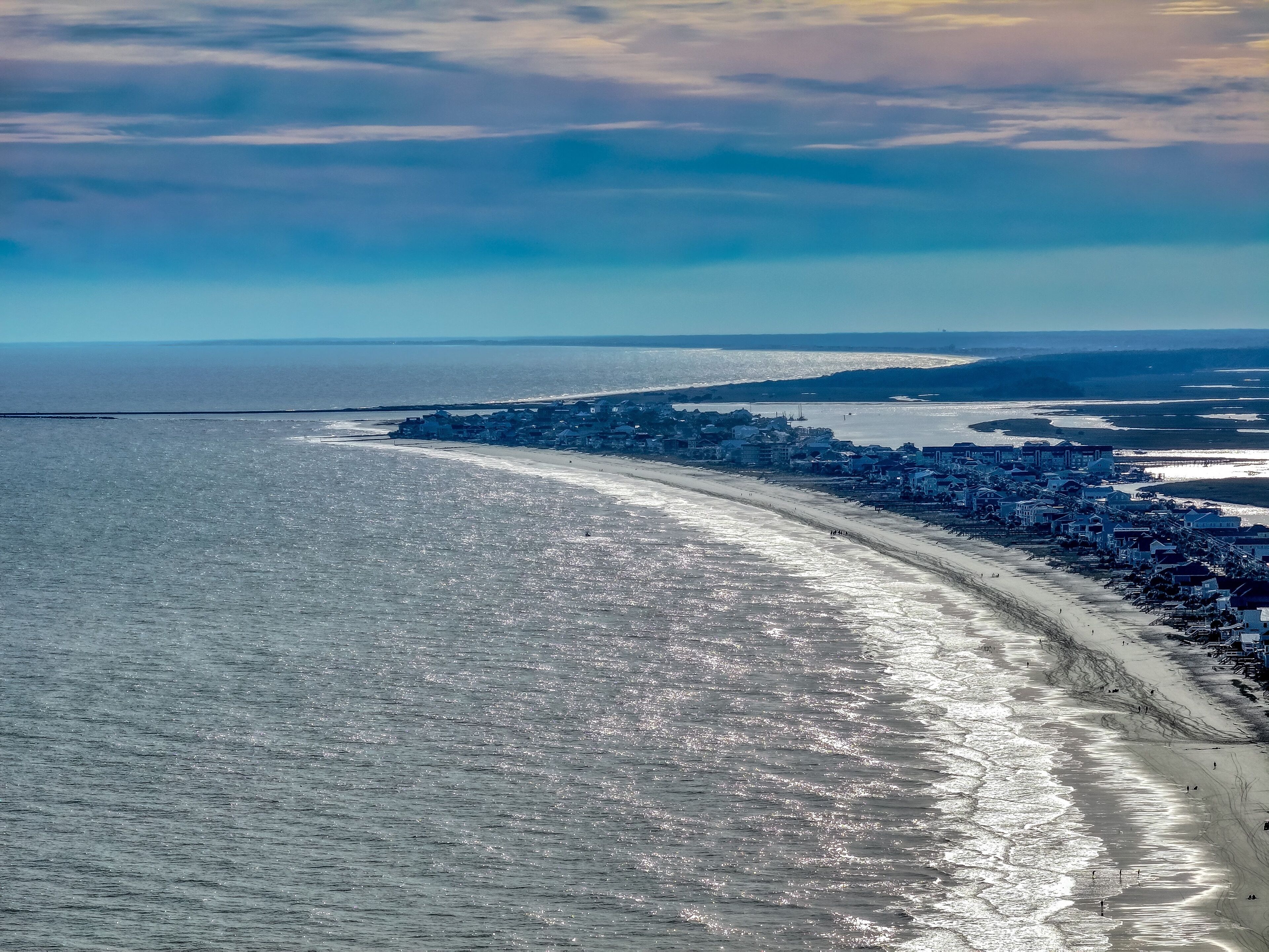 Una vista aerea di una cittadina costiera con una lunga spiaggia, cielo sereno e mare calmo.
