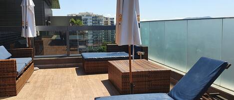A rooftop terrace with wicker furniture, blue cushions, and white umbrellas.