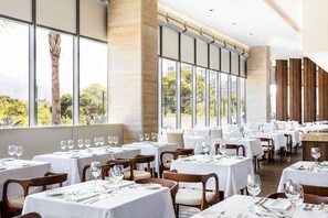 A restaurant with multiple tables set for dining, large windows offering a view of greenery and buildings, and a modern interior design. - SQUARE DESIGN HOTEL (Rio de Janeiro)