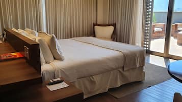 Habitación de hotel con una cama grande, un escritorio con teléfono, control remoto y una computadora portátil. Cuenta con un balcón y muebles de mimbre.