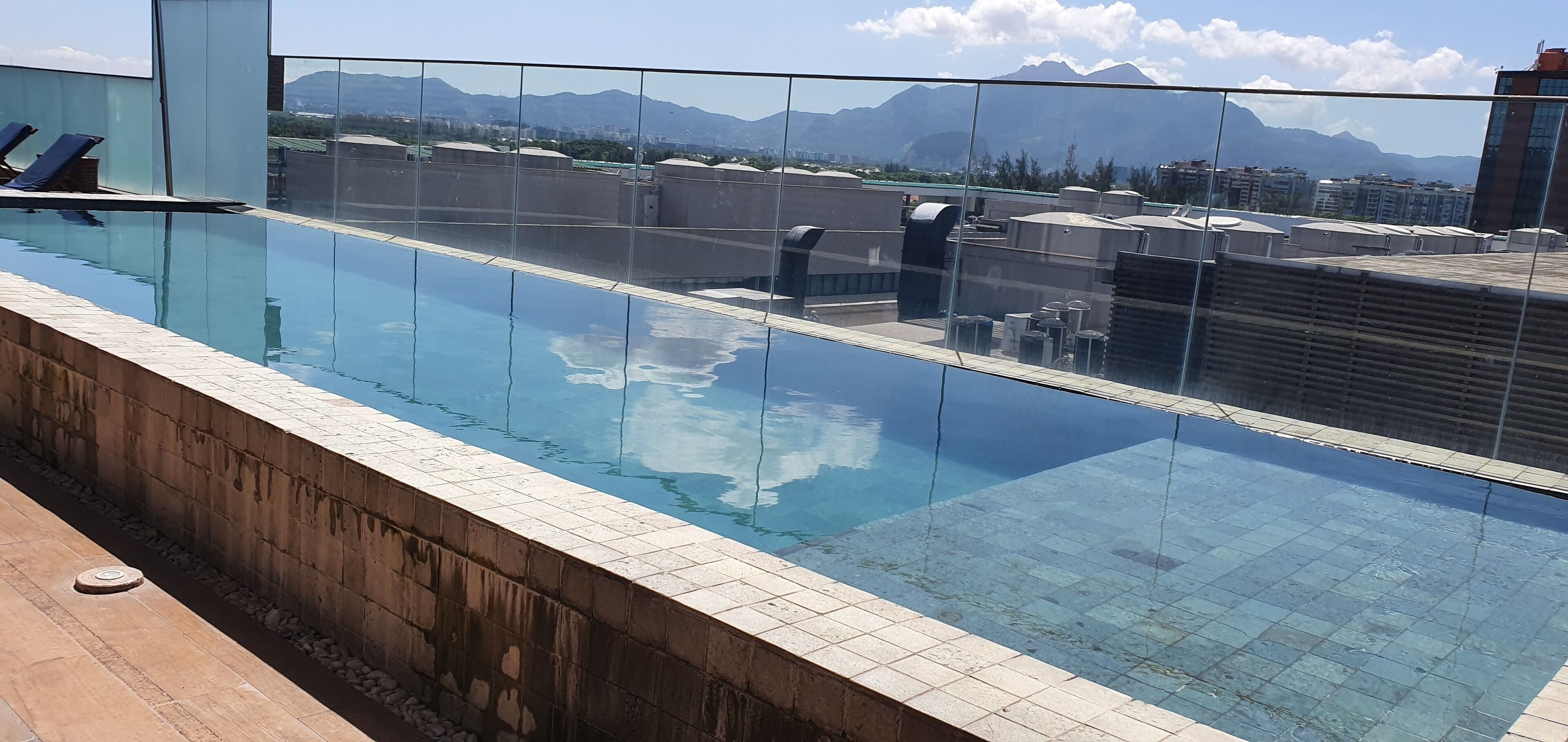Una piscina infinita en la azotea con vistas despejadas a montañas y edificios al fondo.