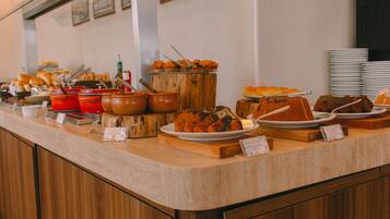 Un banco buffet con diversi cibi esposti, tra cui pasticcini e prodotti da forno, su supporti e piatti di legno.