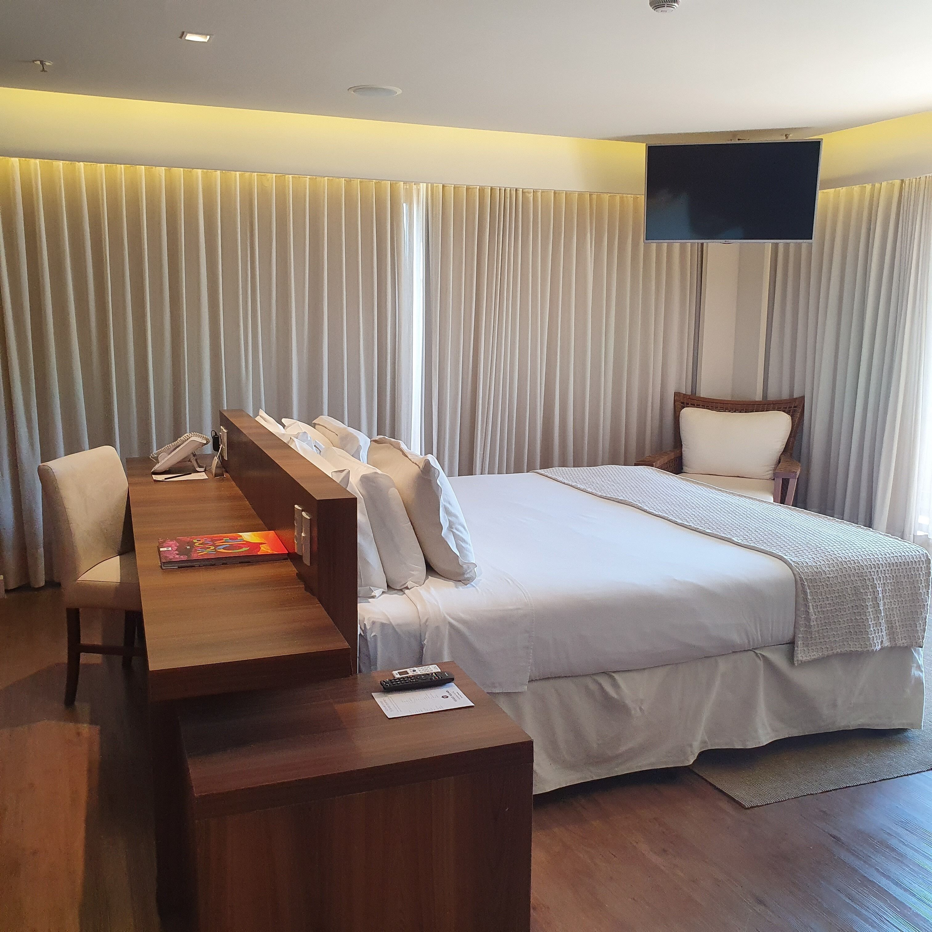 A hotel room with a bed, a desk, a chair, a TV, and curtains.