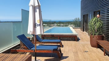Terraço no telhado com duas espreguiçadeiras, piscina e vista para o mar.