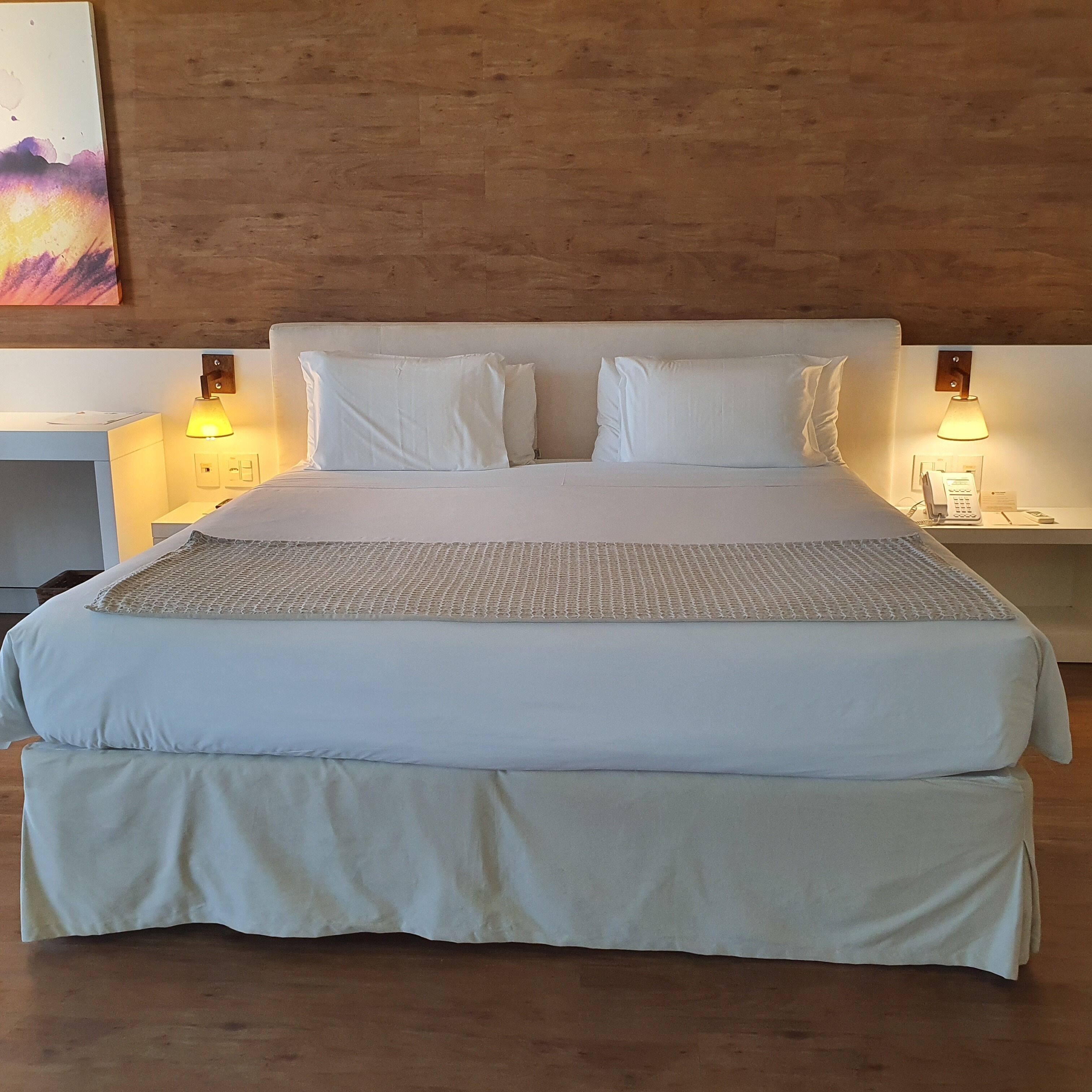 Una cama grande con sábanas blancas, dos mesitas de noche con lámparas y un cabecero de madera.